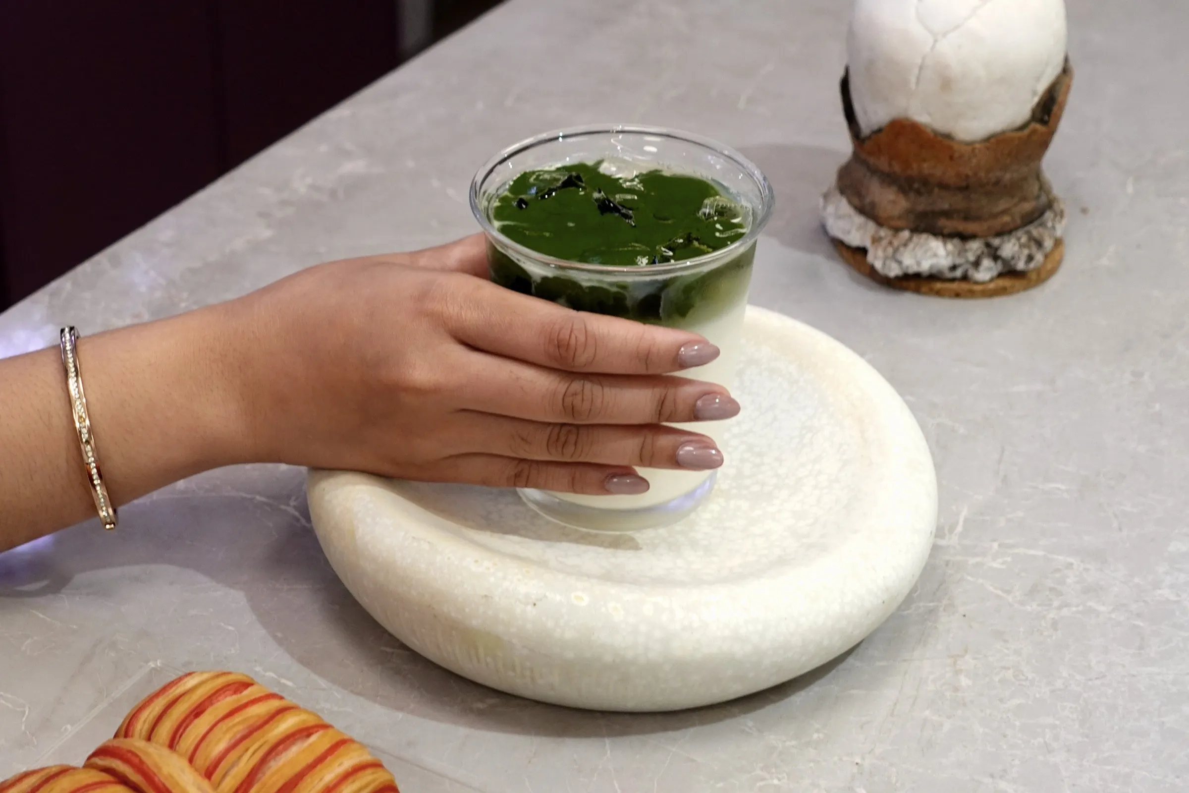 A hand lifting a glass of iced matcha from a stone plate at the Lavande café counter