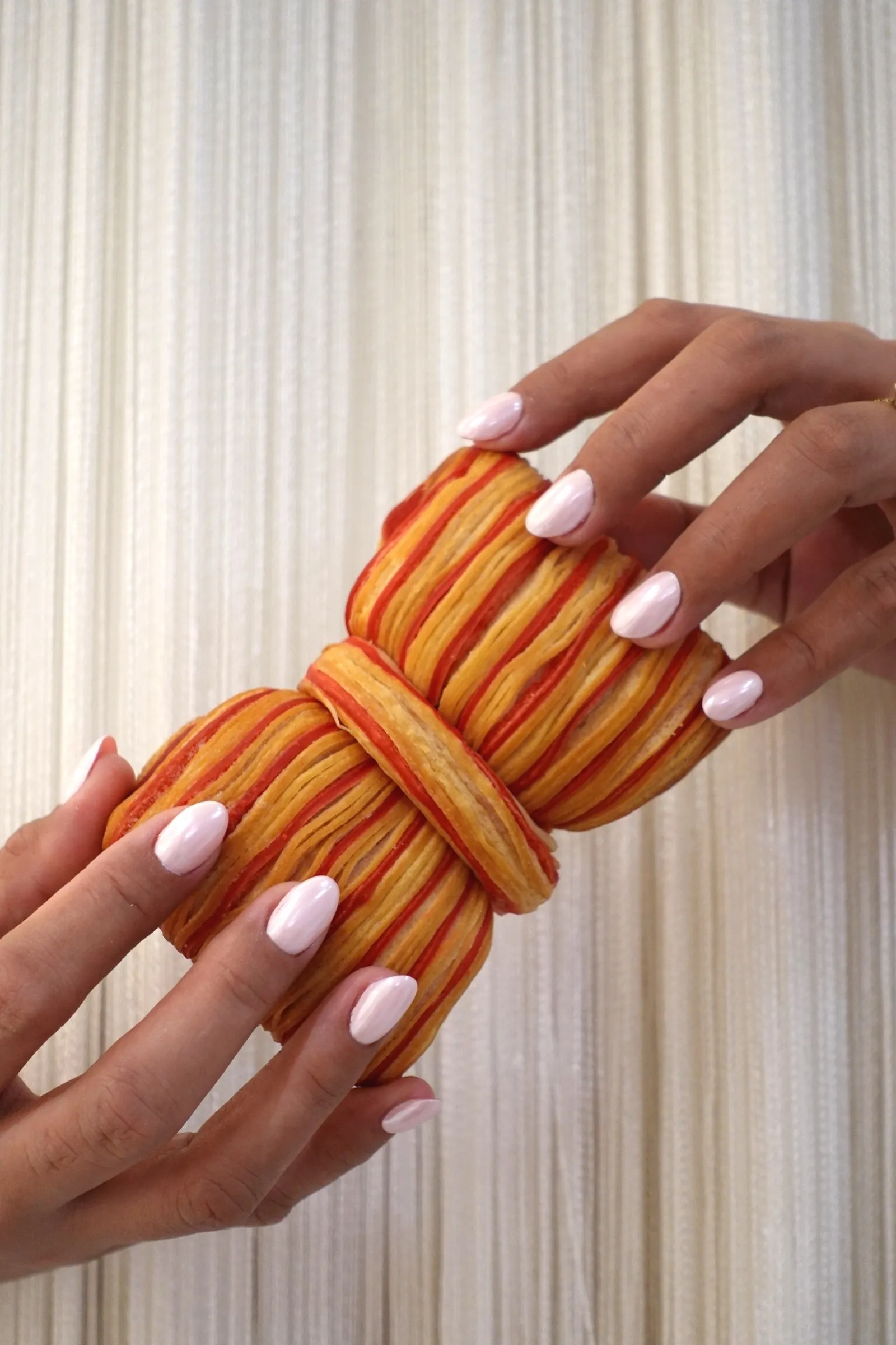 Hands with pale almond nails holding a striped croissant from the Lavande café