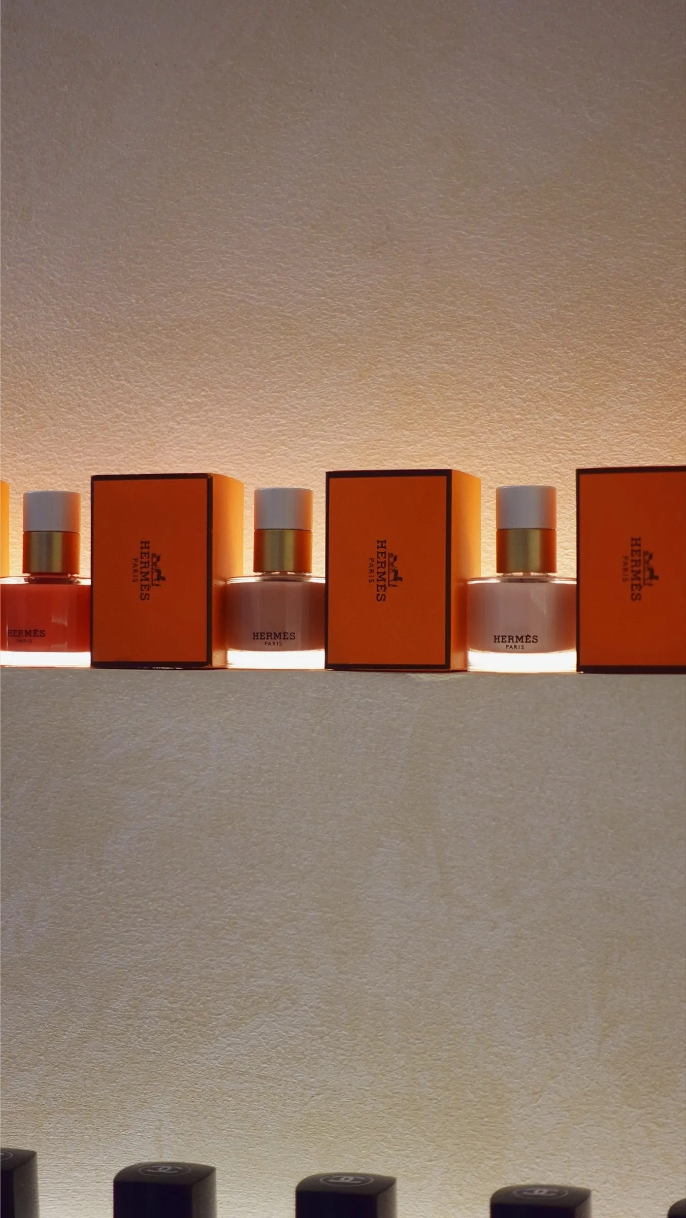 Hermès nail polish bottles beside their orange boxes on a lit plaster shelf at Lavande