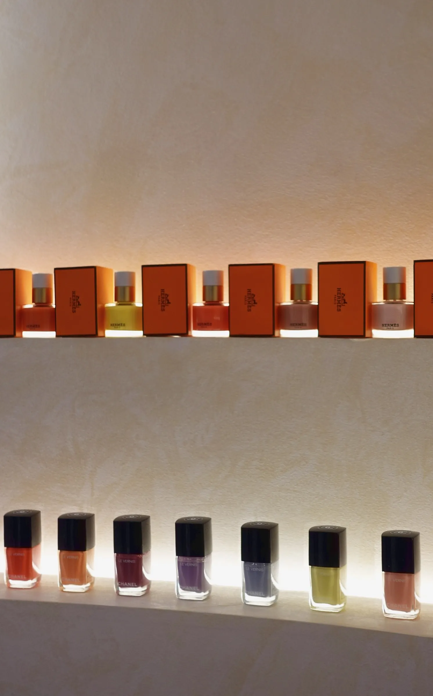 Bottles of Hermès and Chanel nail polish lit on curved plaster shelves at Lavande