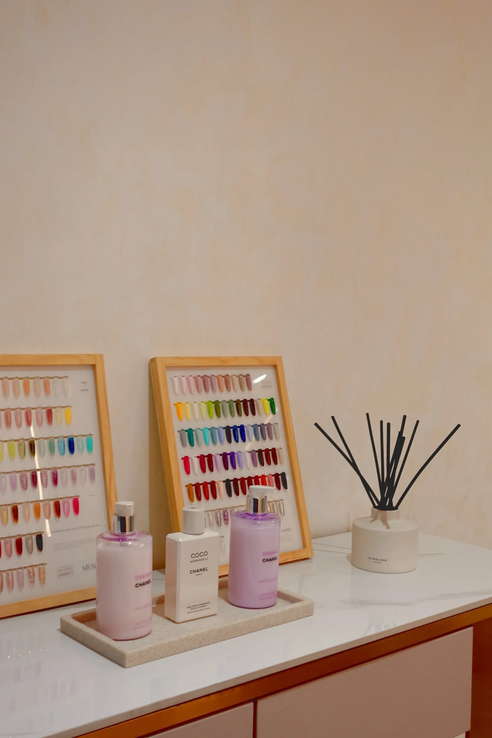 Framed nail colour swatches and a reed diffuser on a white shelf