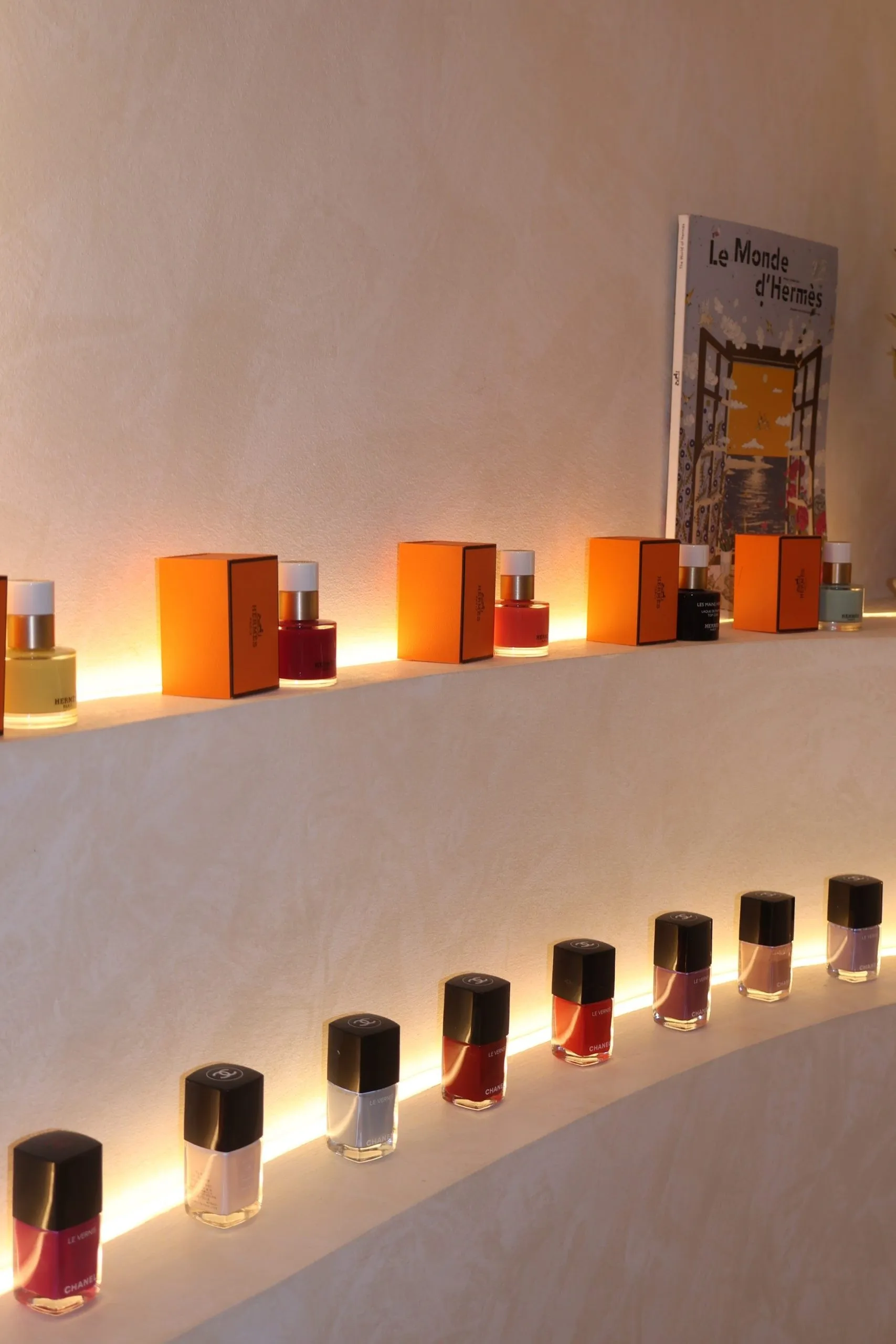 Hermès and Chanel nail polish bottles on a curved, softly lit plaster shelf at Lavande.